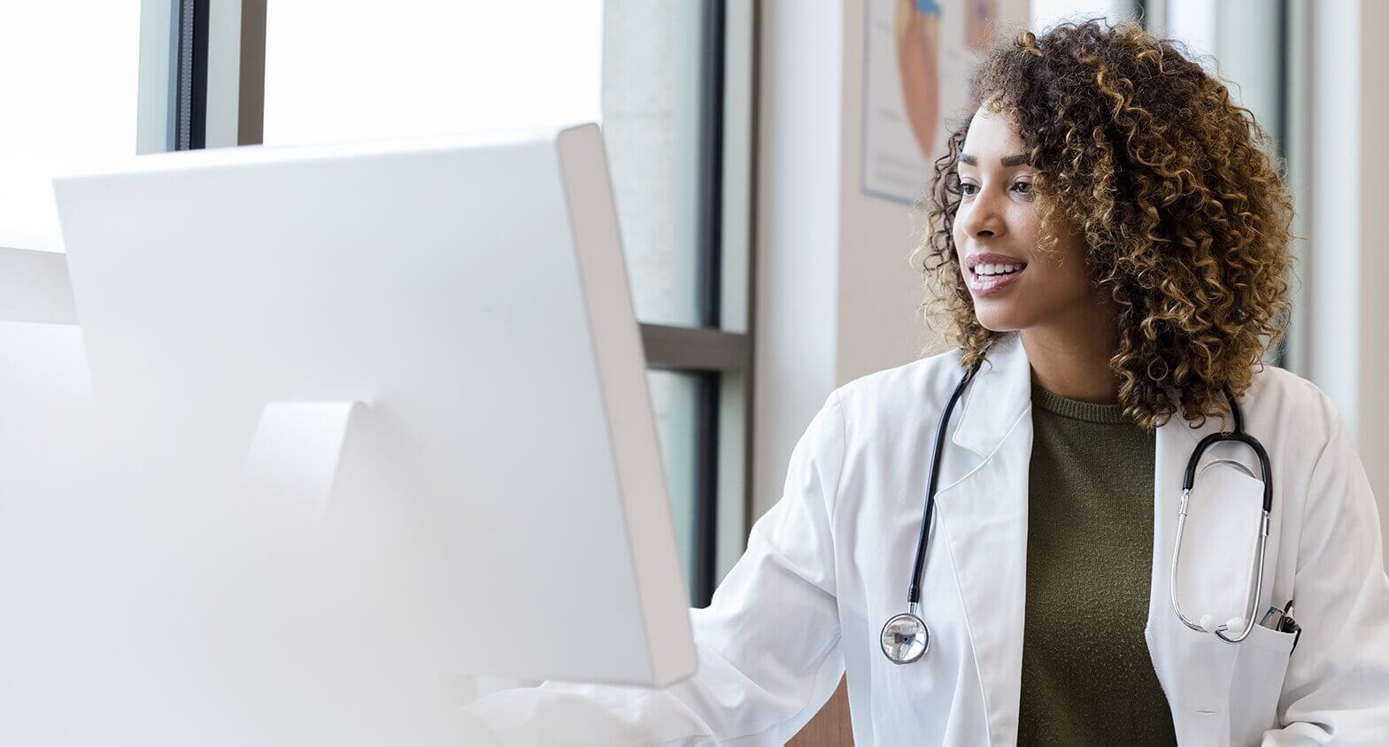 The mid adult female doctor reviews her patient's records on her computer in her office.